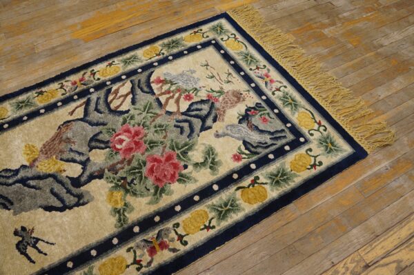 Textured beige rug with pink flowers, blue birds, and a navy border sits on worn wood planks.