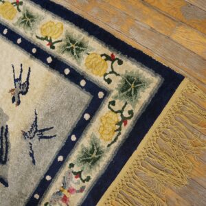 High-pile rug corner shows blue floral borders, a grey field, yellow fringe, and worn plank flooring.