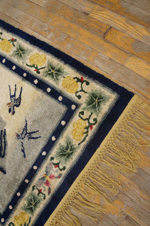 High-pile rug corner shows blue floral borders, a grey field, yellow fringe, and worn plank flooring.