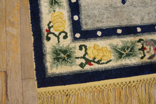Highly textured floral rug with yellow blooms, a navy border, and long gold fringe on wood planks.