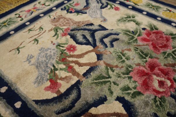 High-pile floral rug detail showing pink flowers, blue birds, green leaves, and navy blue border on a beige field.