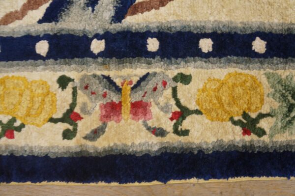 A close-up of a textured rug showing a butterfly and yellow flowers framed by navy blue bands.