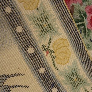 Detail of a tight woven rug with yellow florals and blue stripes over a plush pink and green floral rug.