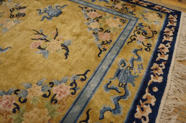 Gold rug with pink, light blue, and dark blue traditional floral motifs and ornate multiple borders.