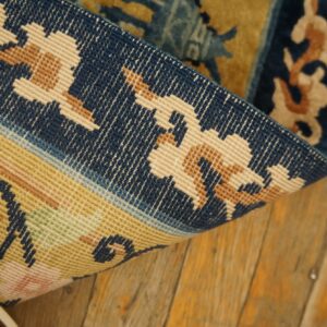 Close view of a blue and gold patterned rug folded on worn plank wood flooring.