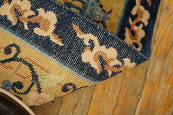 Close view of a blue and gold patterned rug folded on worn plank wood flooring.