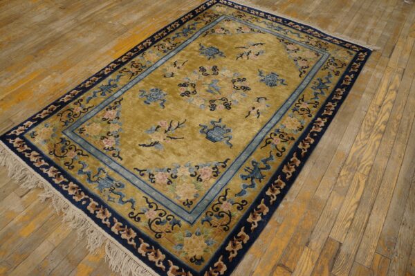 Gold rug with blue borders and traditional floral patterns rests on distressed light wood plank flooring.