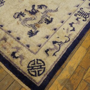 Textured cream rug with dark blue and purple traditional patterns rests on rustic golden hardwood flooring.