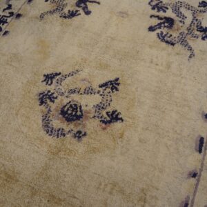 Textured tan rug with faded navy and lavender floral patterns and a dark border over hardwood floorboards.