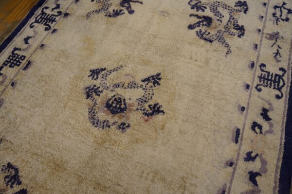 Textured tan rug with faded navy and lavender floral patterns and a dark border over hardwood floorboards.