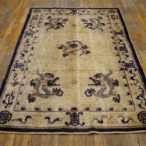 Beige rug featuring a dark blue traditional motif border and field design on worn hardwood planks.