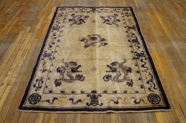 Beige rug featuring a dark blue traditional motif border and field design on worn hardwood planks.