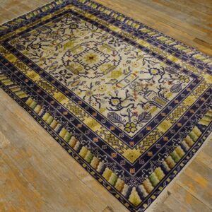 Cream rug with navy blue borders and olive green details sits angled on distressed wood floor.