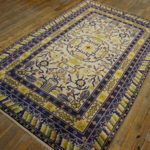 Cream rug with indigo and gold geometric patterns and multi-colored borders lying on distressed wood.