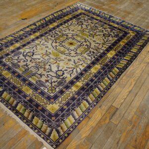 A geometric patterned rug in cream, navy blue, and olive green sits on distressed yellow wood plank flooring.
