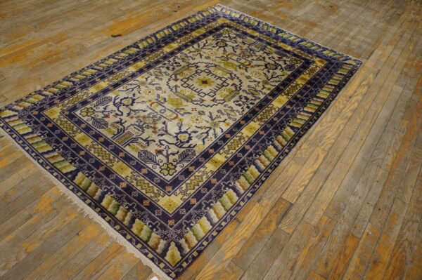 A geometric patterned rug in cream, navy blue, and olive green sits on distressed yellow wood plank flooring.
