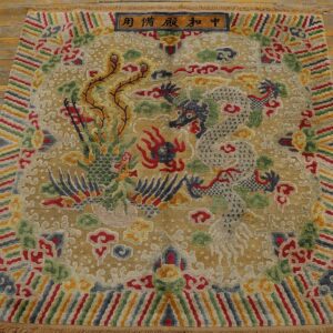 Multi-colored rug with gold background displays a central dragon and phoenix pattern on distressed wood planks.