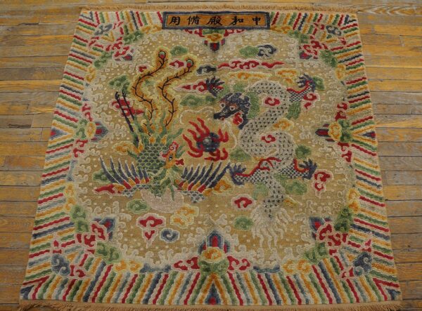 Multi-colored rug with gold background displays a central dragon and phoenix pattern on distressed wood planks.
