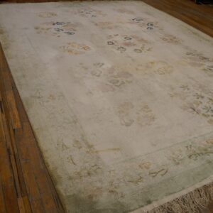 Light floral rug with subtle pastel colors and a sage green border on wood plank floors.