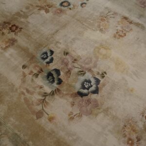 Distressed tan rug featuring large, carved floral motifs in faded shades of blue, pink, and brown.