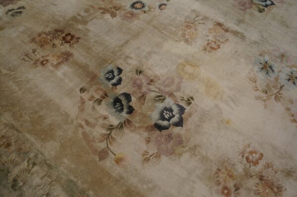 Distressed tan rug featuring large, carved floral motifs in faded shades of blue, pink, and brown.