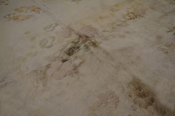 Distressed low-pile rug featuring large floral patterns in pale pink, muted yellow, and beige tones.
