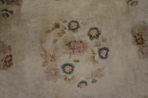 Distressed beige rug featuring an antique-style floral wreath design in muted blues, mauves, and tans.