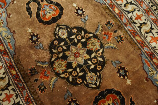 Detailed view of a warm brown rug with complex floral motifs and border elements in black, blue, and orange.