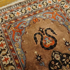 Ornate brown rug with detailed rust and blue gray borders rests on distressed wood flooring.