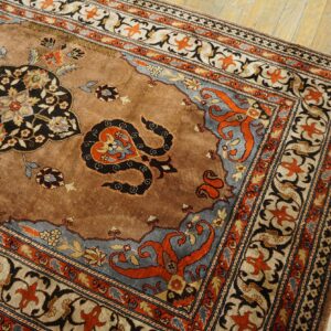 Ornate tan rug featuring black, rust, and slate blue floral medallions rests on light wooden plank floors.