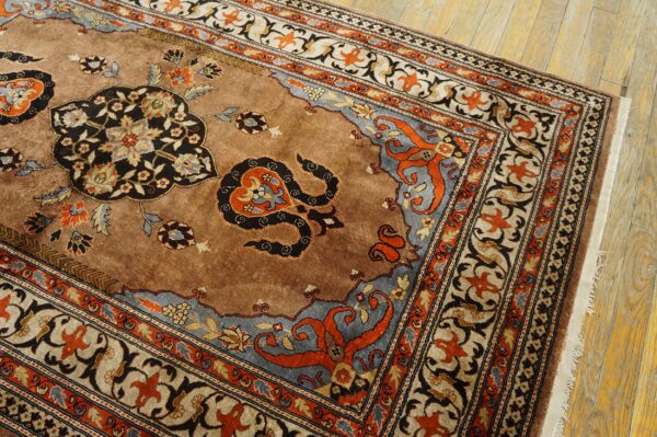 Ornate tan rug featuring black, rust, and slate blue floral medallions rests on light wooden plank floors.