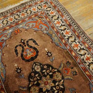 Ornate brown rug featuring black, orange, and blue floral motifs rests on worn light wood flooring.