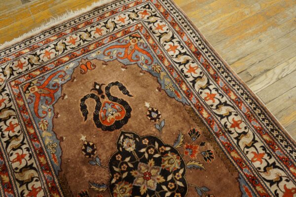 Ornate brown rug featuring black, orange, and blue floral motifs rests on worn light wood flooring.