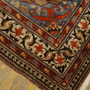Ornate rug corner showing brown, blue, beige, and orange traditional patterns resting on light wood floors.