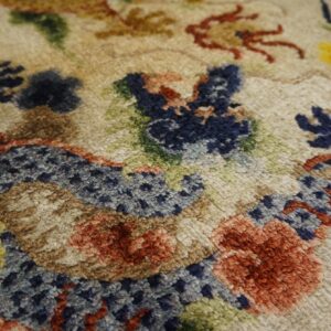 High pile rug texture showing abstract design elements in beige, navy, rust, brown, green, and yellow.