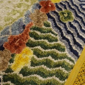 High-pile rug detail showing abstract colorful blocks in rust, green, blue, and yellow with a thick yellow fringe.