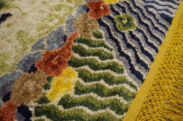 High-pile rug detail showing abstract colorful blocks in rust, green, blue, and yellow with a thick yellow fringe.