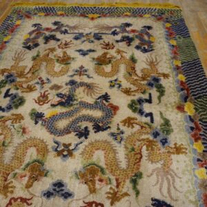Cream rug with gold, blue, and red dragon motifs and a complex wavy border on a rustic hardwood floor.
