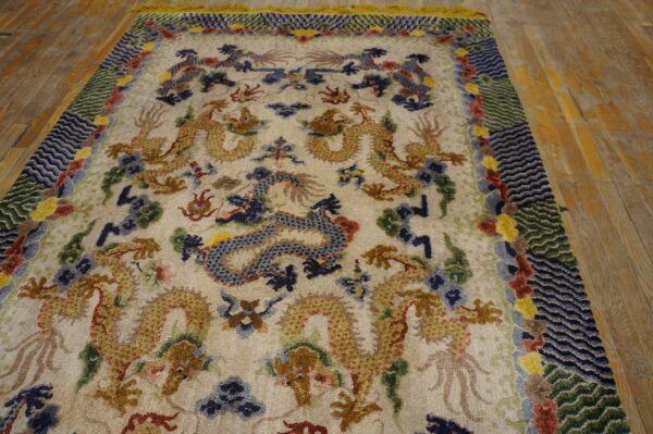 Cream rug with gold, blue, and red dragon motifs and a complex wavy border on a rustic hardwood floor.