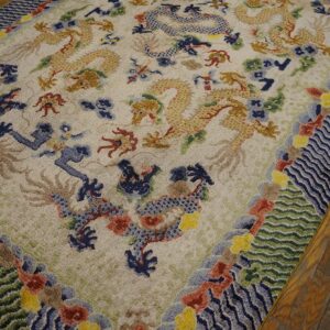 Ornate rug with gold and blue dragons, a complex wave border, resting on dark hardwood floors.