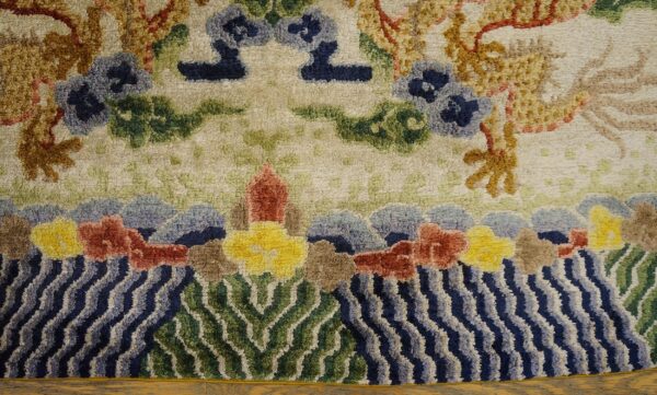 Textured cream rug featuring gold motifs, blue flowers, and a detailed border of wavy blue water and green plants.