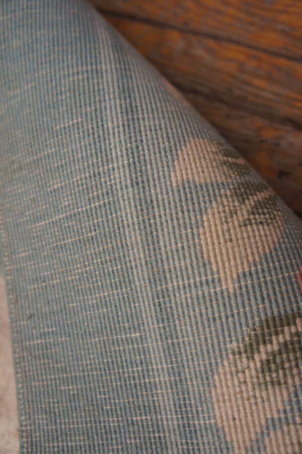 Vintage light cream color european influenced florals luxurious silk pile chinese room size rug 8 Rolled blue and light beige low-pile rug detail showing a ribbed texture against rustic wood planks.