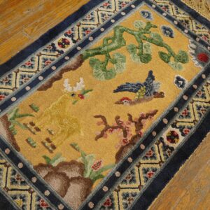 High-pile yellow rug displaying a deer, bird, and vine motif with complex indigo blue outer borders.