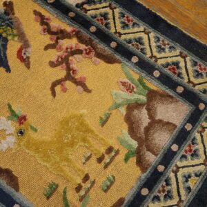 A golden yellow textured rug featuring raised pile deer and bird motifs, framed by a dark blue patterned border on hardwood.