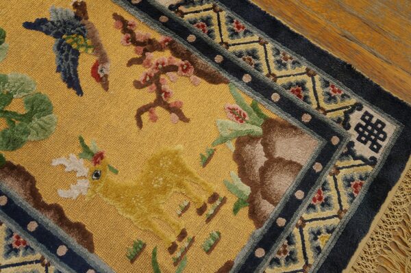 A golden yellow textured rug featuring raised pile deer and bird motifs, framed by a dark blue patterned border on hardwood.