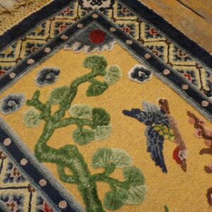 Textured golden rug with raised green tree and bird designs, framed by a patterned navy border on wood.