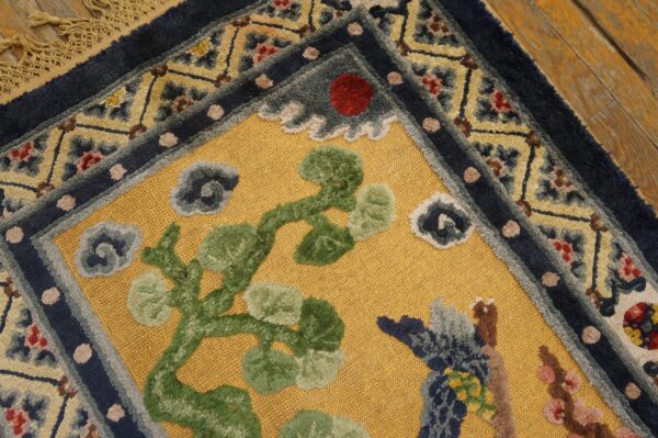 Detailed view of a gold and navy bordered rug featuring green botanical elements on wood flooring.
