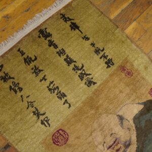 A green and tan rug featuring dark script and a figure design rests on rustic, honey-toned hardwood floors.