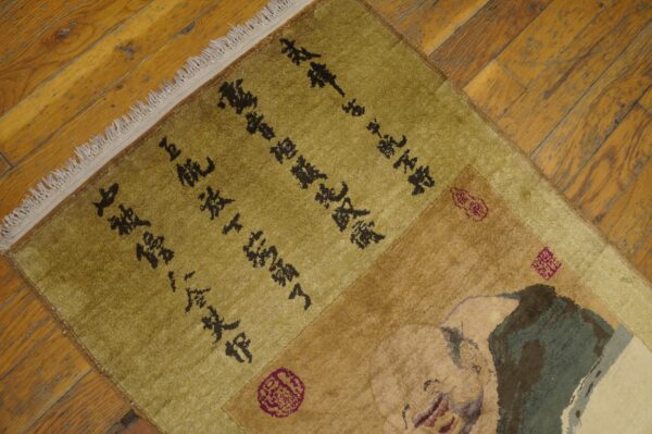 A green and tan rug featuring dark script and a figure design rests on rustic, honey-toned hardwood floors.