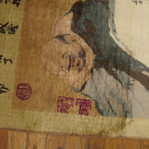 Distressed green, tan, and cream rug featuring a figure portrait, calligraphy, and magenta seal motifs rests on wood floor.